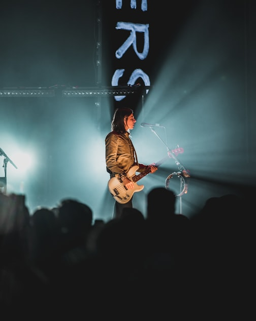 A musician plays an electric guitar and sings on stage, illuminated by dramatic lighting, with a crowd watching in the foreground—capturing a moment as dynamic and engaging as a full service marketing agency bringing creative visions to life.