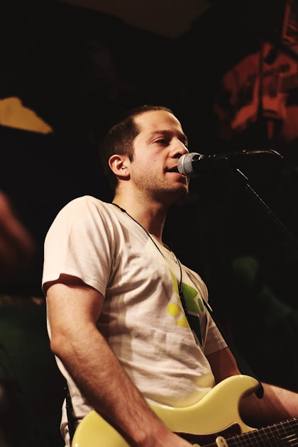 A man wearing a white t-shirt plays an electric guitar and sings into a microphone on stage, with dim lighting and a dark background—capturing the creative spirit you’d expect from a leading San Diego web design company.