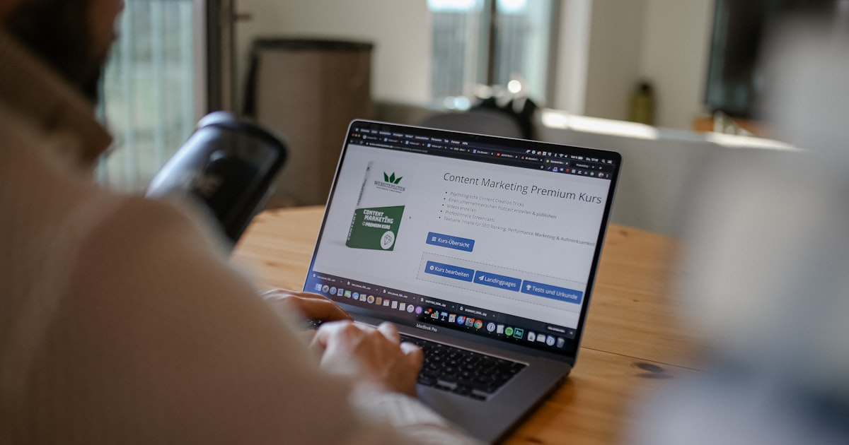 Person using a laptop at a wooden table, viewing a webpage for a Content Marketing Premium Kurs with course material and signup options visible on the screen, offered by a full service marketing agency known for its effective content marketing packages.