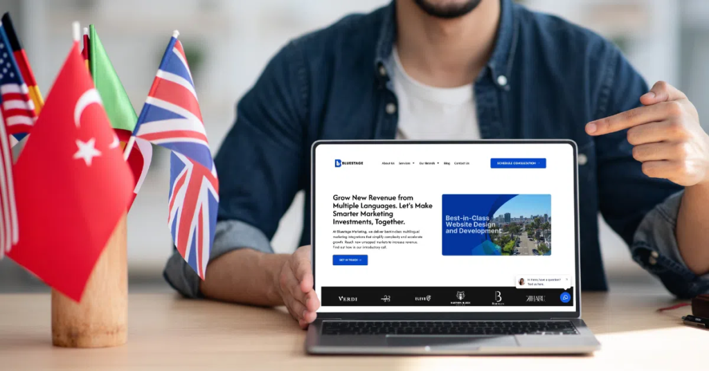 A person points at a laptop displaying a business website, sitting at a table with small flags of Turkey, France, Italy, the UK, and the US—an ideal setting for an international digital marketing agency. The background is blurred.