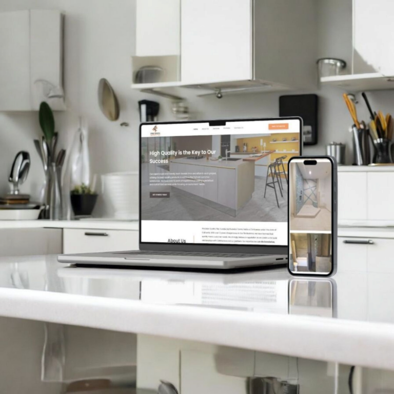 A laptop and a smartphone displaying a website are placed on a glossy kitchen counter, with modern white cabinets, utensils, and kitchen tools visible in the background—highlighting how seamlessly a digital marketing agency can bring your brand to life across multiple devices.